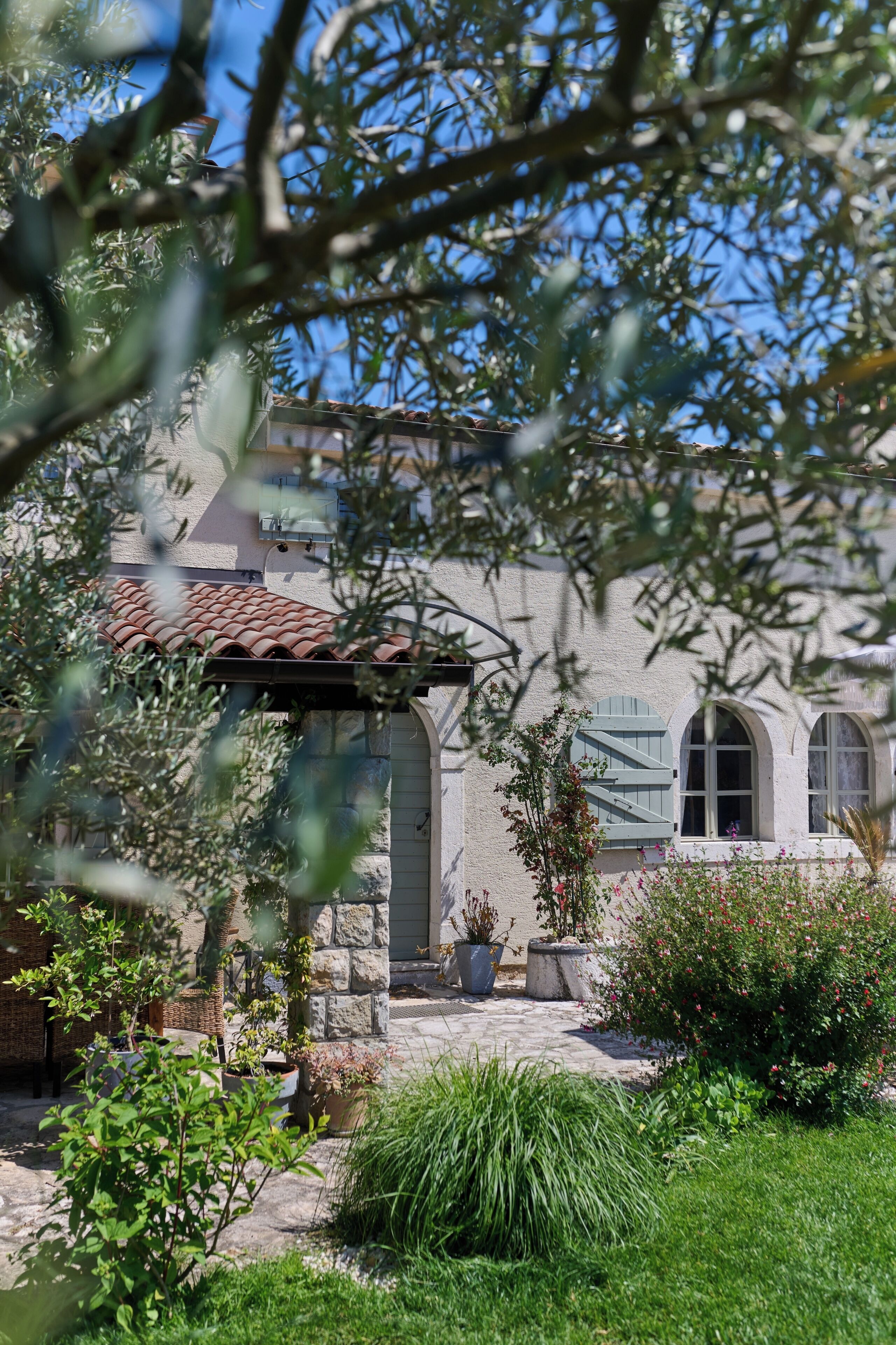 Ein Gebäude aus Stein mit einem Ziegeldach, Bogenfenstern und einem Garten mit Topfpflanzen und Sträuchern.