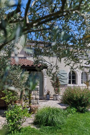 Ein Gebäude aus Stein mit einem Ziegeldach, Bogenfenstern und einem Garten mit Topfpflanzen und Sträuchern.