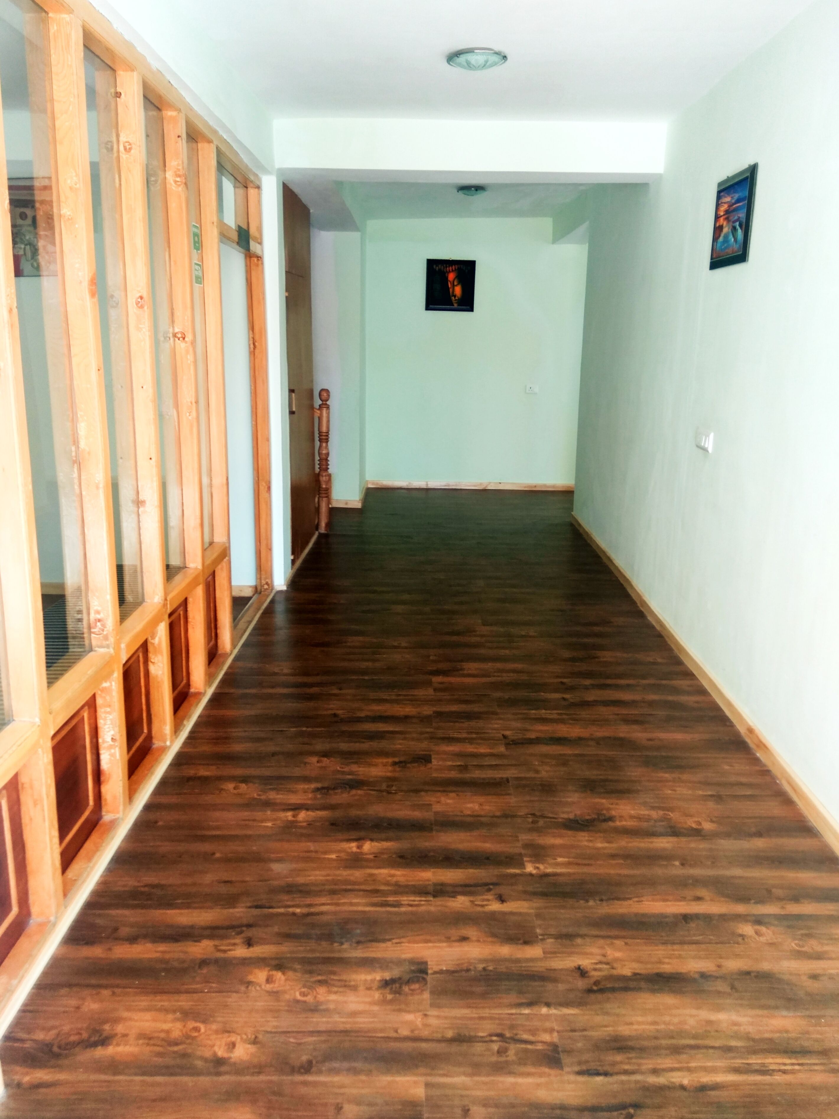 A hallway with wooden flooring and glass doors on the left.