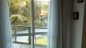 A hotel room with a sliding glass door leading to a balcony with a view of palm trees and a building in the background. - Anchor Flat Resort, beachfront, 2 km from the village of Porto de Galinhas, sleeps 6.  (Ipojuca - Porto de Galinhas)