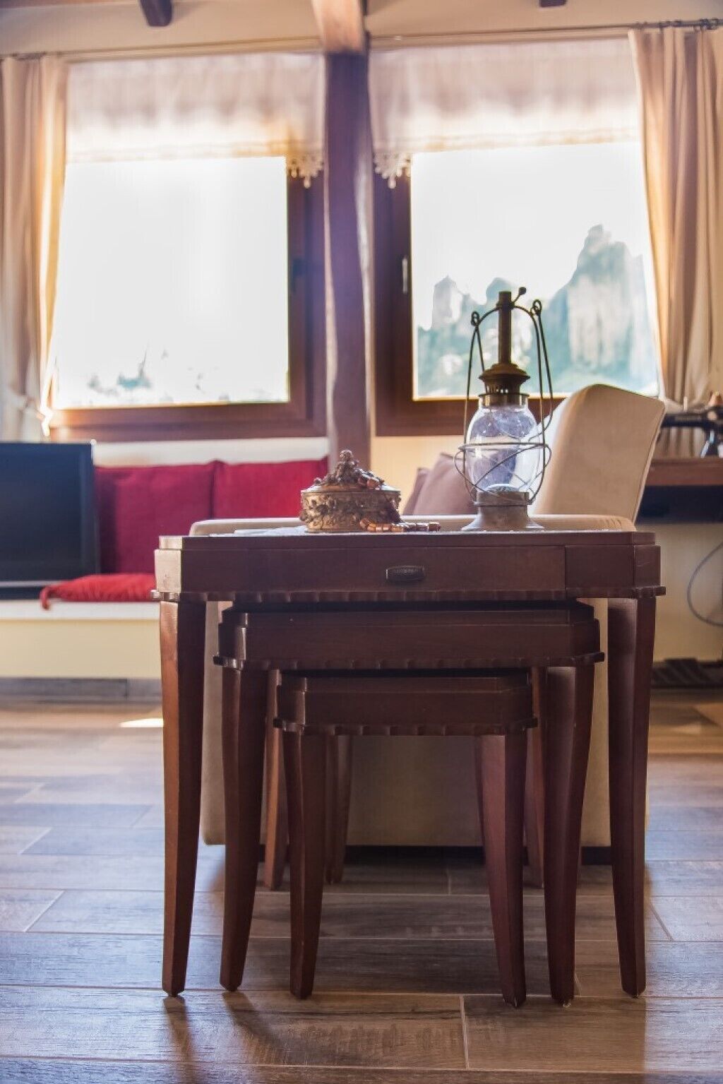 A wooden table with a lamp and a decorative item on it, positioned in front of a window with curtains.