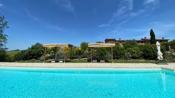Ein klares, blaues Schwimmbecken mit Liegestühlen und einer Pergola.