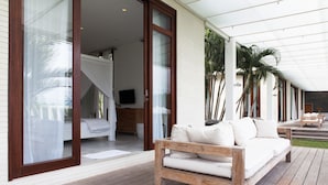 Un espacio exterior moderno con terraza de madera, sofá blanco y cama con dosel.