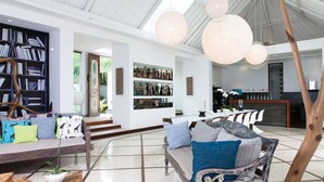 Amplia sala de estar con una gran estantería, un comedor con una mesa larga y una cocina moderna al fondo.