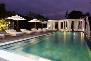 An outdoor swimming pool with lounge chairs and umbrellas, surrounded by greenery. - Wholesome Luxury 7BR Villa, Canggu - w/ Spacious Pool & Lounging Area! (Canggu)