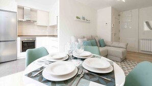 A modern kitchen with built-in appliances, a dining area with a round table set for four, and a living area with a sofa and cushions. - Seattle | The Rentals Collection (San Sebastián)