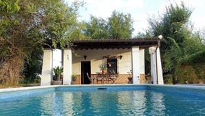 Una piscina con zona de terraza, rodeada de árboles.