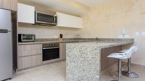 A modern kitchen with a granite countertop, built-in oven, microwave, and a stainless steel refrigerator. There are two bar stools and a knife block on the counter. - Jungle Tulum Condo, Rooftop Jacuzzi, Pool & Views (Tulum)
