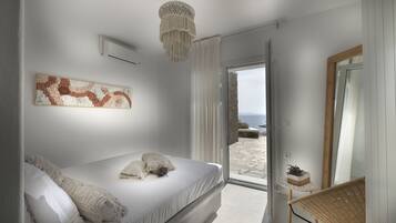 A bedroom with a bed, a chandelier, a view of the outdoors, and a wicker chair.