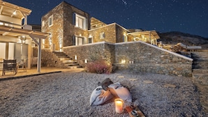 A stone house with a patio area at night, featuring a candle and a cup on a tray. - Simousi Villas (Kithnos)