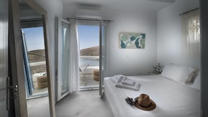 A bedroom with a bed, a hat, and a view of the sea through open doors. - Simousi Villas (Kithnos)