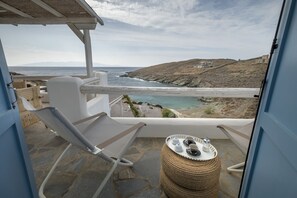 A balcony with a view of the sea, stone flooring, a wicker table with cups, and a cushioned chair. - Simousi Villas (Kithnos)