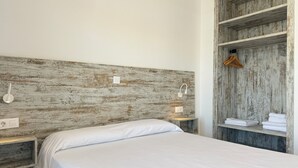 A bedroom with a wooden headboard, a bed with white bedding, bedside lamps, a wooden nightstand, and a wooden wardrobe with folded towels. - Agi Rescator 101 Apartamento for rent in Roses Girona. (Roses)