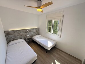 Een kamer met twee bedden, een plafondventilator, een raam en een houten hoofdeinde.