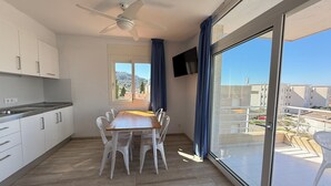 A modern kitchen with white cabinets, a dining table with chairs, a ceiling fan, and a large sliding glass door to a balcony. - Agi Rescator 101 Apartamento for rent in Roses Girona. (Roses)
