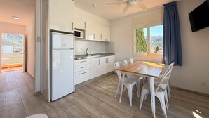 A modern kitchen with white cabinets, a microwave, and a dining area with a wooden table and white chairs. - Agi Rescator 101 Apartamento for rent in Roses Girona. (Roses)