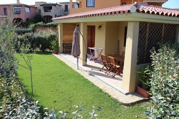 Une terrasse avec une table et des chaises, un petit jardin et un bâtiment doté d’un toit en tuiles.