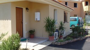 A residential building with a wooden door, a white air conditioning unit, and a turquoise van parked outside. - SHORT TERM LET IN SARDINIA, HOLIDAY HOME OLBIA-PITTULONGU WITHIN 5MIN FROM BEACH (Olbia)