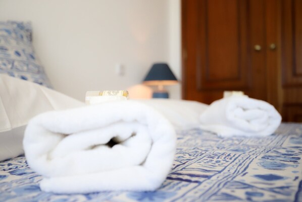 A neatly made bed with rolled white towels, a bedside table with a lamp, and a wooden wardrobe in the background. - Sotto Mayor Residence (Figueira da Foz)