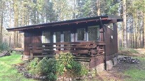 A cabin with a wooden deck, stone foundation, and a forest backdrop. - SKERRY is an authentic log cabin in a lovely forest location close to Loch Awe (Taynuilt)