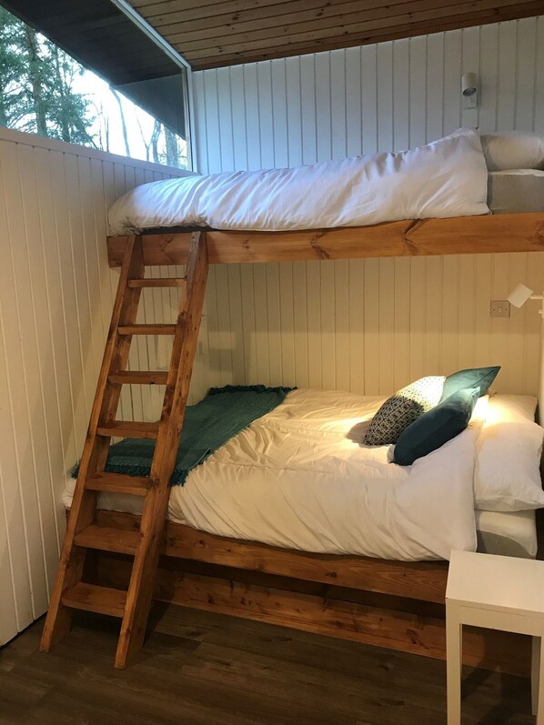 Ein Stockbett mit einer Holzleiter, weißer Bettwäsche und einer türkisblauen Decke.