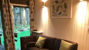 A cozy living room with a brown leather sofa, a wooden coffee table, and a painting on the wall. - SKERRY is an authentic log cabin in a lovely forest location close to Loch Awe (Taynuilt)