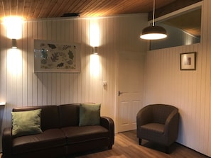 Ein Zimmer mit einem braunen Ledersofa, einem grünen Kissen, einem grauen Sessel und einem gerahmten Kunstwerk an der Wand.