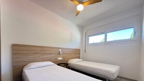 Ett hotellrum med två separata sängar, en sänggavel i trä, en takfläkt, ett fönster med utsikt och ett litet runt bord.