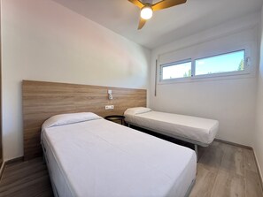 Una camera d'albergo con due letti singoli, una testiera in legno, una ventola a soffitto, una finestra con vista e un piccolo tavolino rotondo.