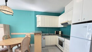 Eine Küche mit weißen Schränken, einer Mikrowelle, einem Kühlschrank und einem Esstisch mit Stühlen.