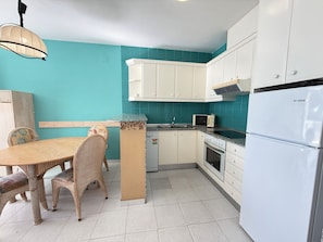 A kitchen with white cabinets, a microwave, a refrigerator, and a dining table with chairs.