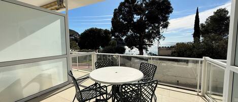 A balcony with a round table and four chairs, overlooking a scenic view of trees and a body of water.