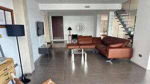 A modern living room with a brown leather sofa, a wooden chair with a fur seat, and a glass coffee table. - Agi Joan Margarit 84B Casa for rent in Roses Girona. (Rosas / Roses)