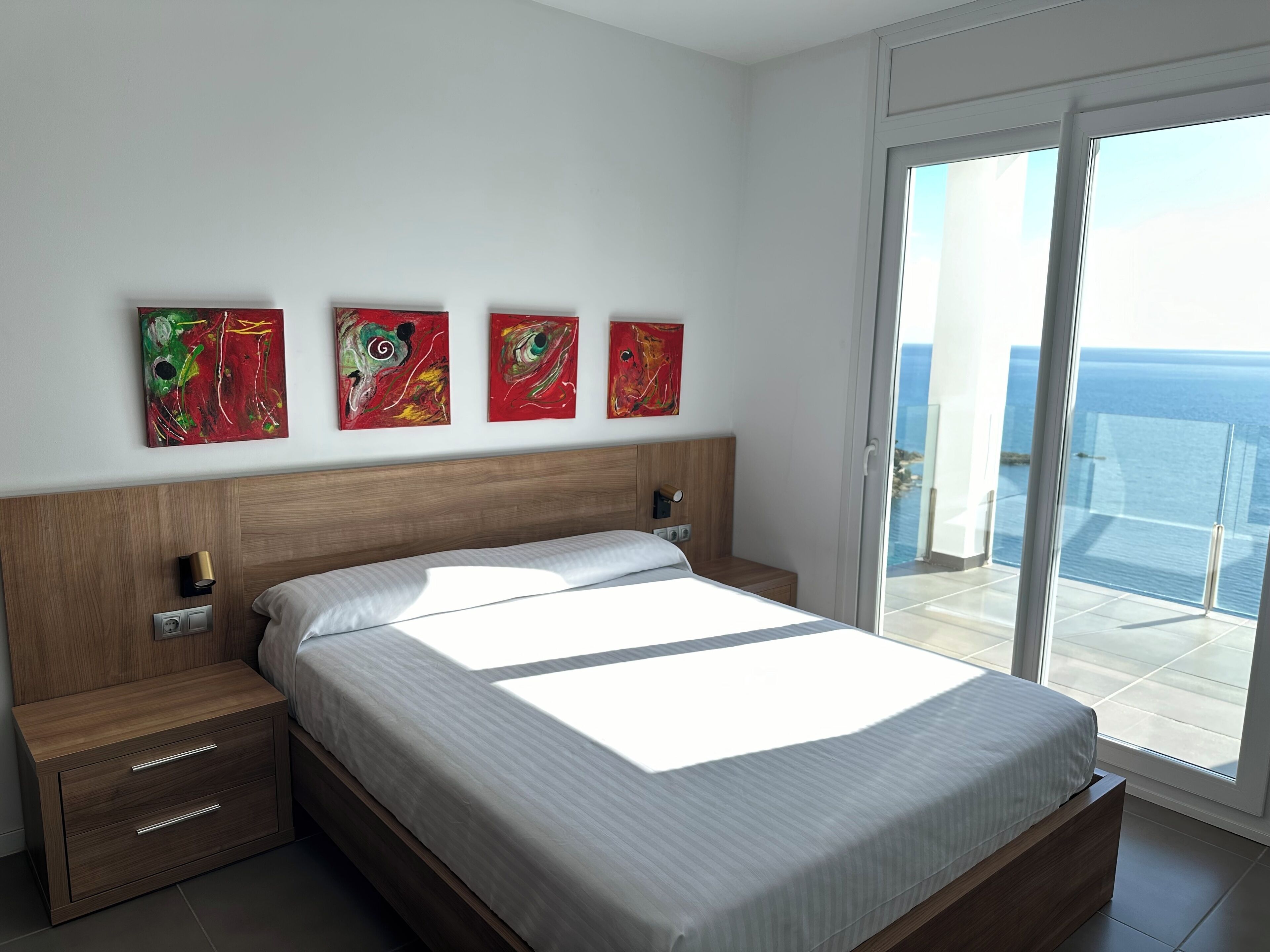 Une chambre moderne avec un grand lit, une table de chevet, une commode et une vue sur l’océan grâce à une porte-fenêtre coulissante.