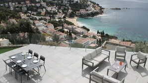 A terrace with a dining table and chairs, a sofa, and a pool table, overlooking a coastal town and beach. - Agi Joan Margarit 84B Casa for rent in Roses Girona. (Rosas / Roses)