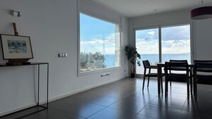 A spacious room with large windows offering a view of the sea, a dining area with chairs, and a potted plant. - Agi Joan Margarit 84B Casa for rent in Roses Girona. (Rosas / Roses)