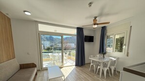 Ein modernes Wohnzimmer mit einer Couch, einem Esstisch mit Stühlen, einem Deckenventilator und einem an der Wand befestigten Fernseher.