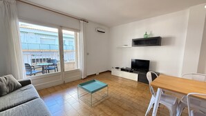 Uma sala de estar moderna com sofá, mesa de jantar e TV. Possui uma varanda com mobiliário de exterior.