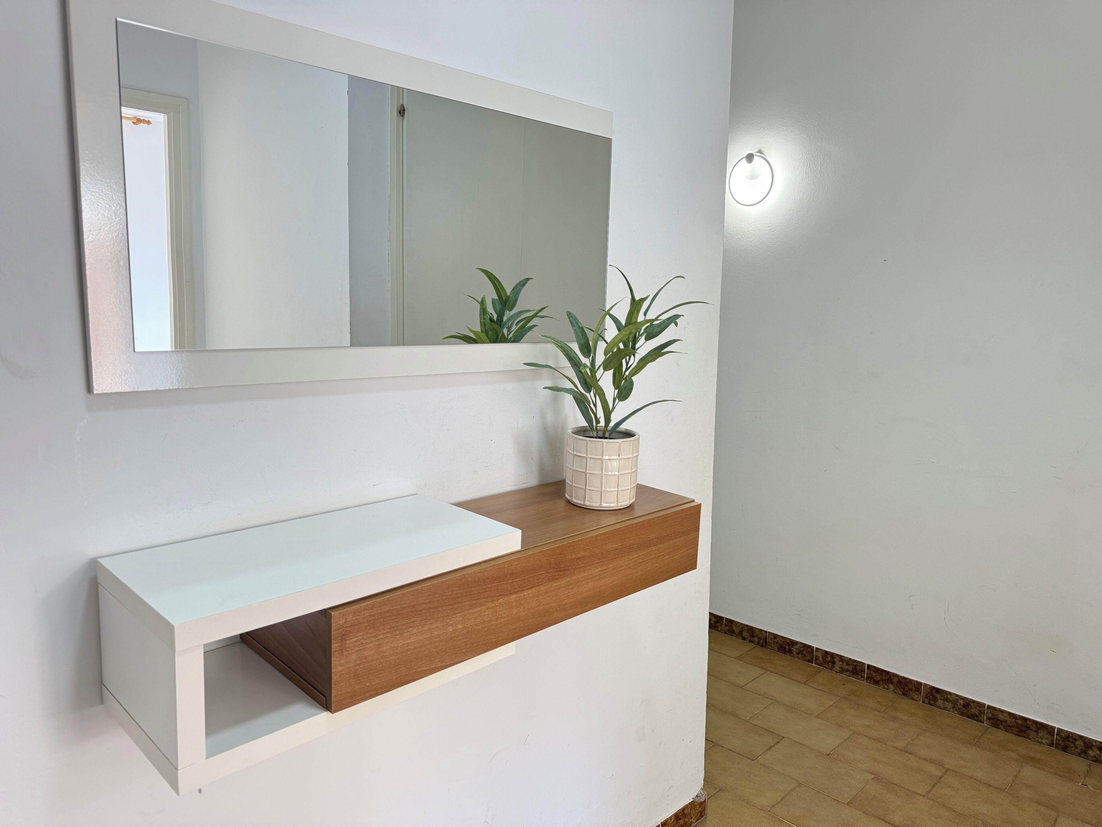Un baño moderno con tocador blanco, un espejo y una planta en maceta.