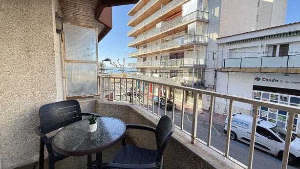 Uma varanda com mesa e cadeiras, com vista para uma rua com carros e edifícios.