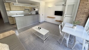 Ett modernt kök med vita skåp, en inbyggd ugn och en mikrovågsugn. Det finns en matplats med ett vitt bord och stolar, och en liten krukväxt på bordet.