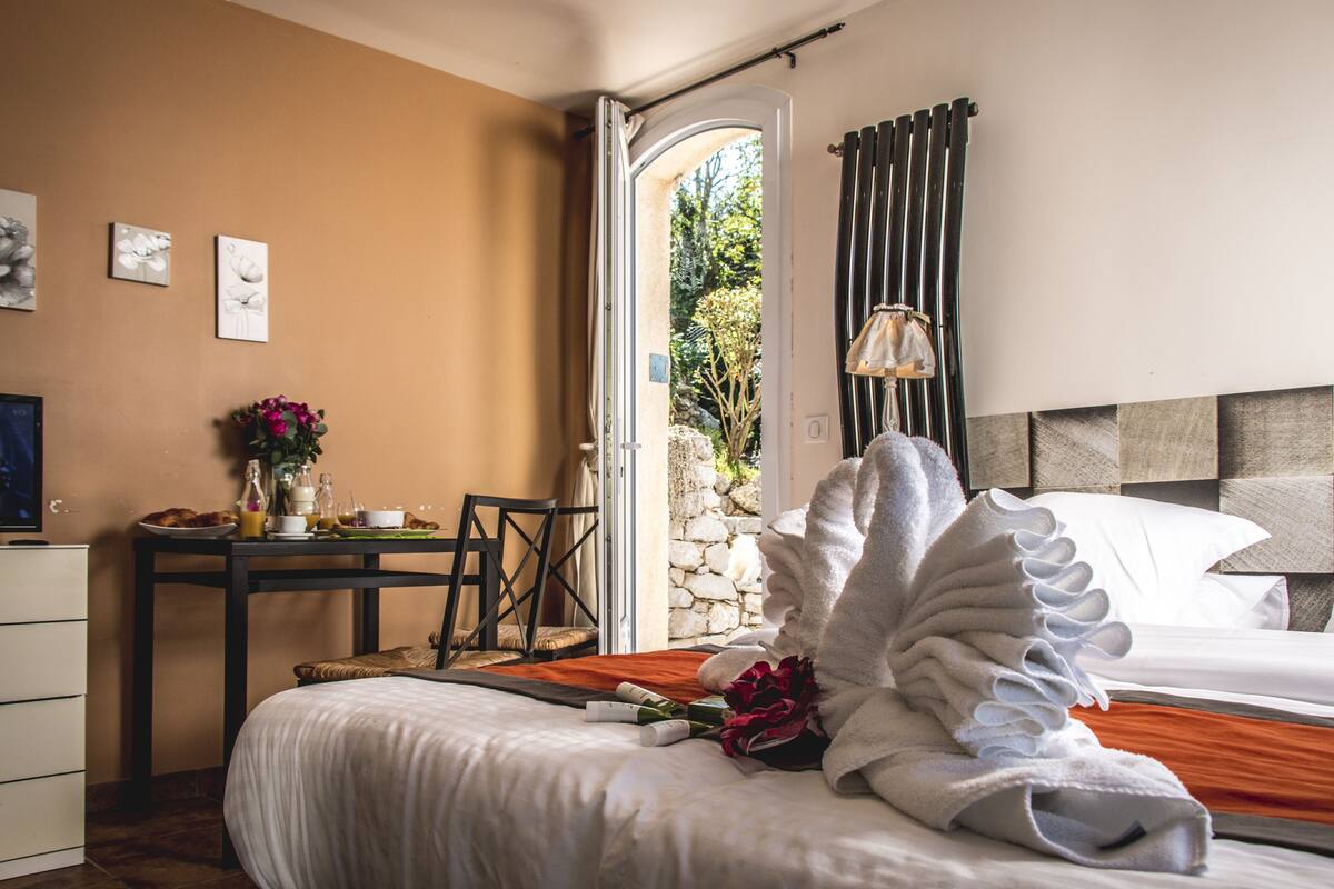 A hotel room with a bed, a desk with breakfast items, a chair, and a view of the outdoors.