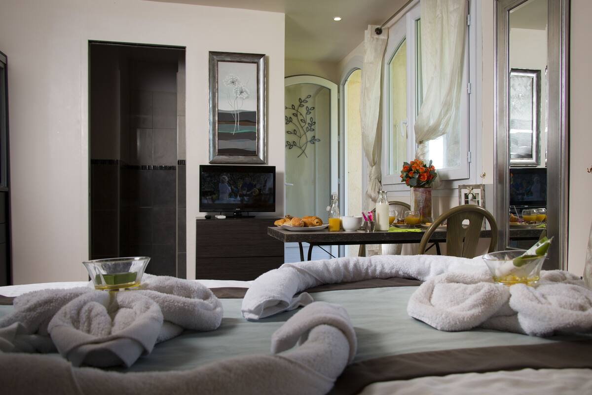 A hotel room with a bed, a television, a dining table with breakfast items, and a bathroom with a shower and toilet.