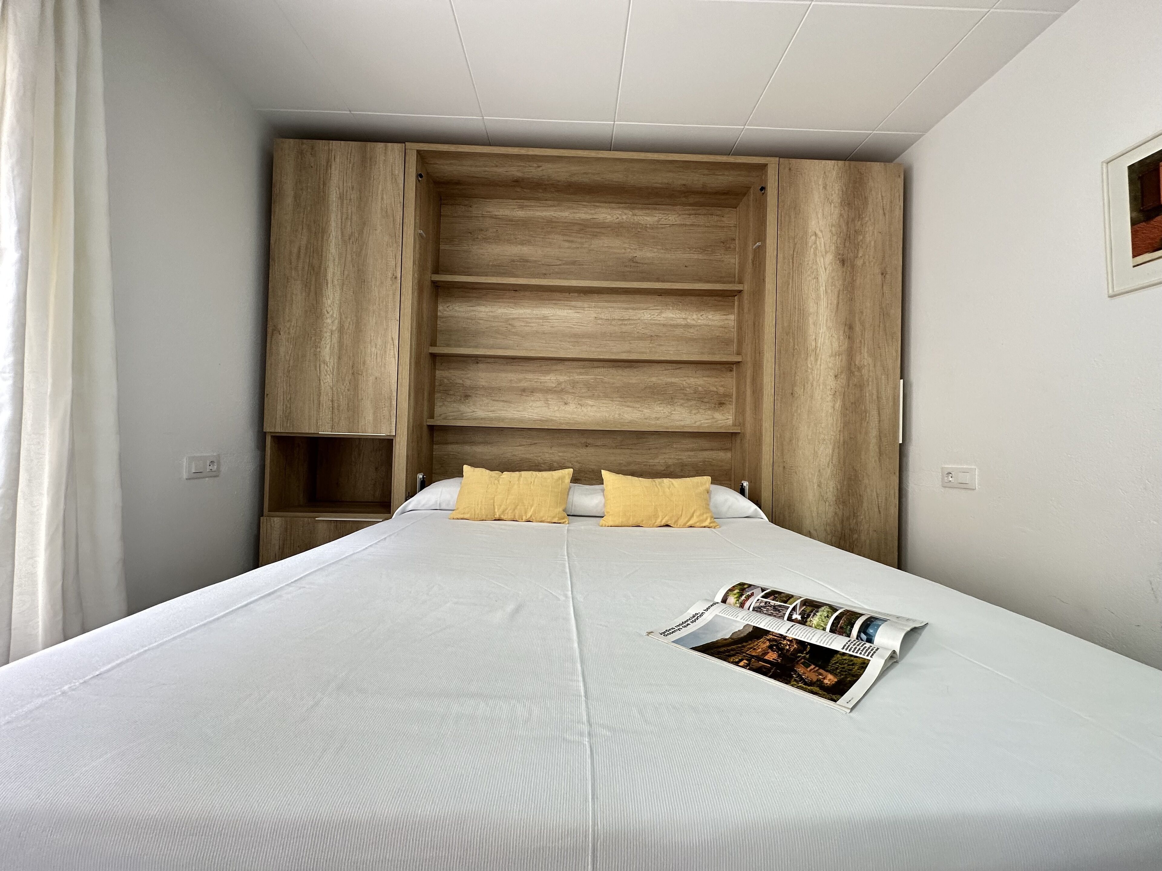 A bedroom with a large bed, wooden headboard, and a magazine on the bed.
