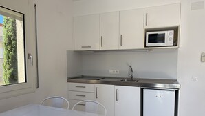 Eine kleine Küche mit weißen Schränken, einer Mikrowelle, einem Spülbecken und einem kleinen Kühlschrank.
