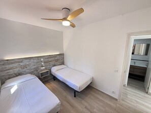 A bedroom with two single beds, a ceiling fan, a bedside table, and a nightstand.