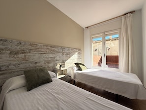 Quarto com duas camas, cabeceira de madeira, mesa de cabeceira e janela com cortinas.