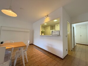 Uma cozinha compacta com micro-ondas, uma janela pequena e uma mesa de jantar de madeira com cadeiras.
