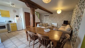 A cozy living room with a wooden dining table and chairs, a sofa, and a TV. - Two Bedroom House in Domaine les Granges (Ternant)