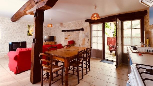 A rustic interior with a stone wall, wooden dining table, red sofa, and a kitchen area with a gas stove. - Two Bedroom House in Domaine les Granges (Ternant)
